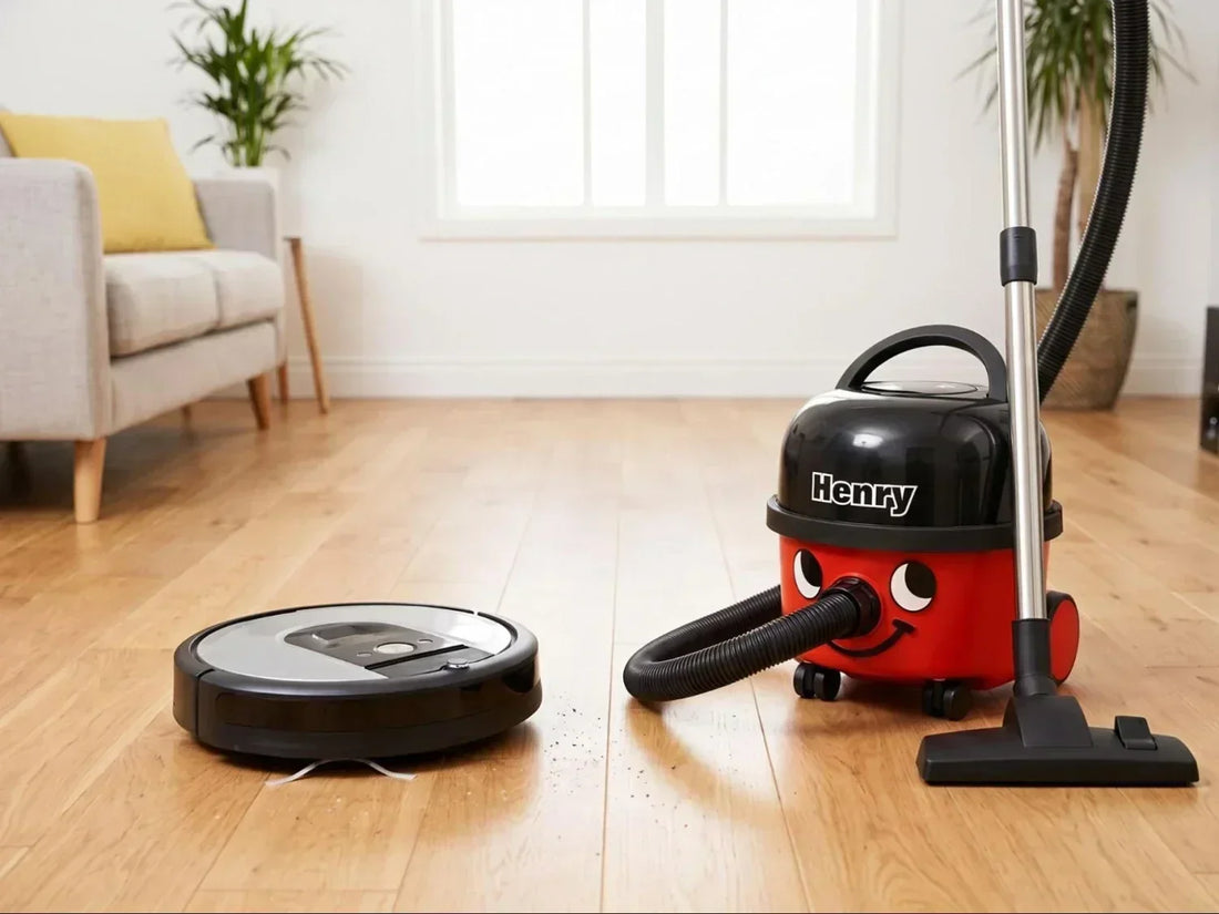 A modern robot vacuum and a Henry vacuum cleaner side-by-side on a hardwood floor.