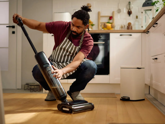 A man in an apron crouching down while checking a damaged vacuum cleaner