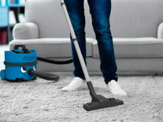  A person using a Henry James vacuum on a carpet