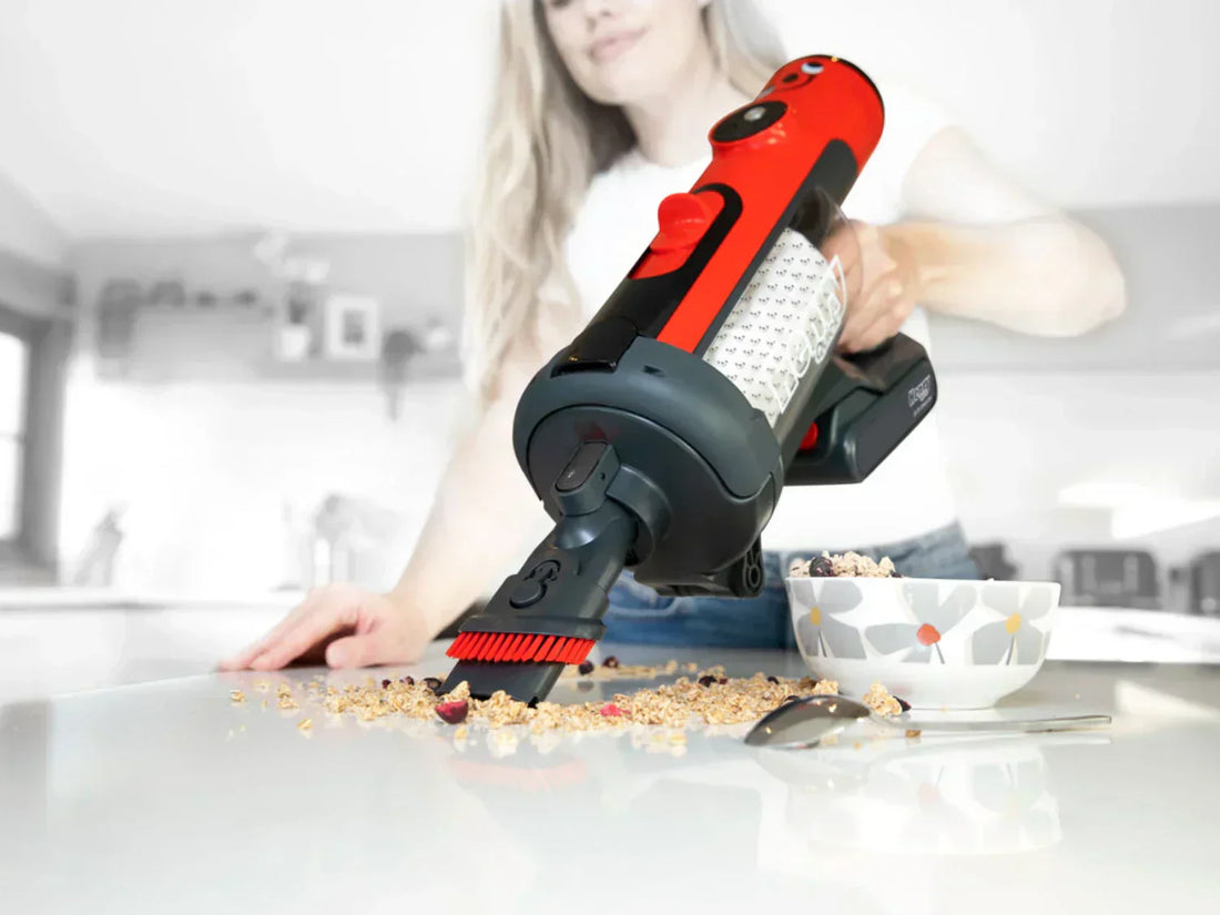 A woman using a handheld vacuum cleaner to clean spilled cereal on a counter